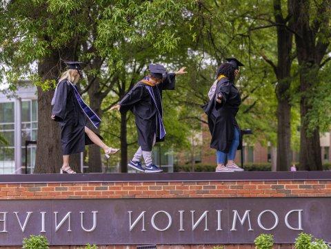 three odu students walk across the ODU sign in caps and gowns